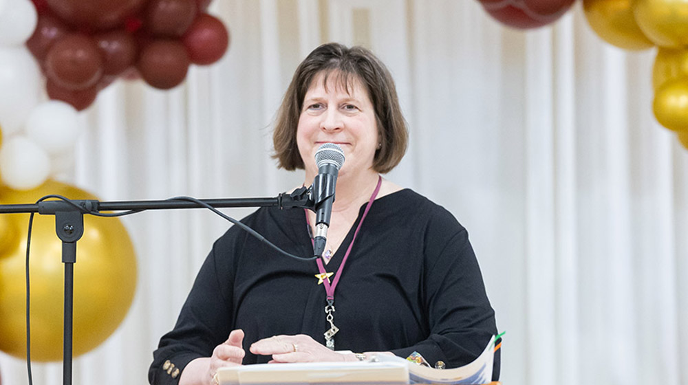 Dr. Theresa Kristopaitis standing behind a microphone and smiling
